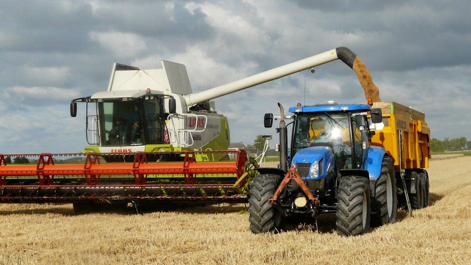 November 2025 Wheat Market Update A modern combine harvester and tractor working together to harvest wheat in a sunny outdoor field.